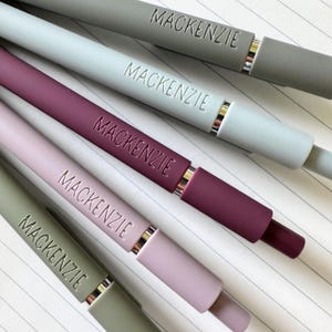 K&ouml;nnte beinhalten: F&uuml;nf Stifte mit dem eingravierten Namen Mackenzie. Die Stifte sind in verschiedenen Farben: grau, hellblau, burgunderrot, helllila und gr&uuml;n.