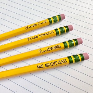 May include: Four yellow pencils with green and black striped erasers. The pencils are labeled with names: Charlotte Carroll, Rylan Edwards, Noa Edwards, and Mrs. Miller's Class.