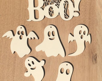 May include: A set of five wooden ghost ornaments with different facial expressions. The ghosts are painted white and have a rustic, unfinished look. The set also includes a wooden sign that says "BOO!" with a spiderweb design.