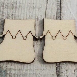 Peut inclure: Deux chaussures d'elfe en bois non finies avec une pointe pointue et un talon recourbé. Les chaussures ont un bord festonné en haut.