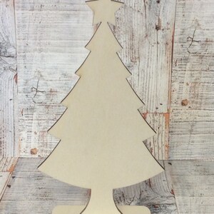 May include: A wooden Christmas tree cutout with a star on top. The tree is standing on a base and is ready to be decorated.