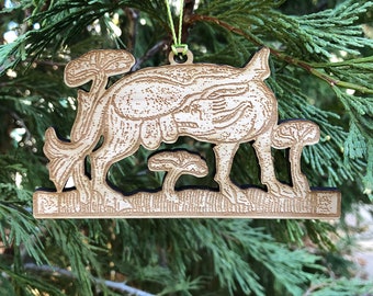 Könnte beinhalten: Ein hölzerner Weihnachtsschmuck mit einem stilisierten Hirsch mit Pilzen. Der Schmuck ist hellbraun mit einem dunklen Rand und einer grünen Schnur zum Aufhängen. Der Schmuck befindet sich vor einem Hintergrund aus grünen Tannennadeln.