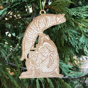 May include: A wooden Christmas ornament featuring a stylized dragon design. The ornament is light brown with intricate etched details, including scales and a curled tail. It hangs from a green string, perfect for holiday decor.