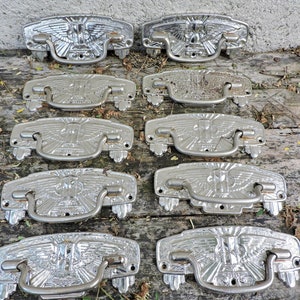 Può includere: Dieci tiretti per cassetti antichi color argento con un designo a forma di aquila. I tiretti hanno un design in rilievo e sono in buone condizioni.