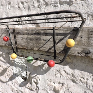 May include: A metal coat rack with five hooks, each with a different coloured ball. The balls are red, yellow, green, yellow, and red. The rack is mounted on a wall with a wooden board behind it.