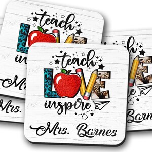 May include: Four white coasters with a woodgrain pattern. Each coaster features a red apple, a yellow pencil, and the words "teach love inspire" in black text. The coasters are personalized with the name "Mrs. Barnes".