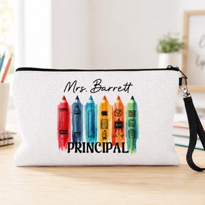 May include: White canvas pencil case with a black zipper and wrist strap. The design features colorful pencil illustrations and the words "Mrs. Barrett PRINCIPAL" in black lettering.