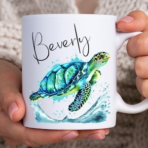 May include: White ceramic mug with a watercolor illustration of a sea turtle swimming in blue water. The name "Beverly" is written in black cursive above the turtle.