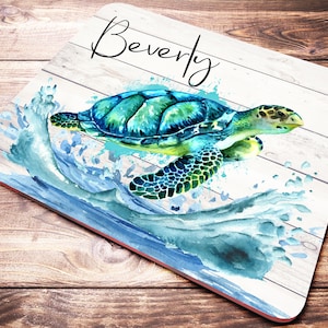 May include: A white wooden coaster with a watercolor painting of a green sea turtle swimming in blue water. The name "Beverly" is written in black cursive at the top of the coaster.