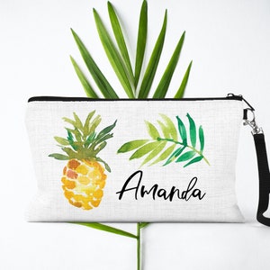 May include: White canvas zippered pouch with a black zipper and a black strap. The pouch has a watercolor illustration of a pineapple and a palm frond. The name "Amanda" is written in black cursive lettering.