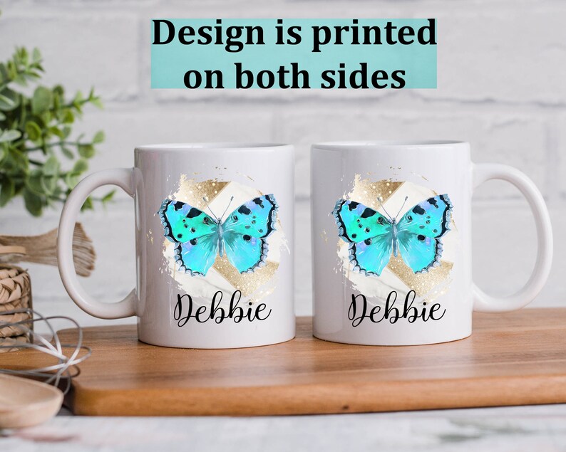 May include: Two white ceramic mugs with a blue butterfly design and gold accents. The mugs have the name "Debbie" printed on them.