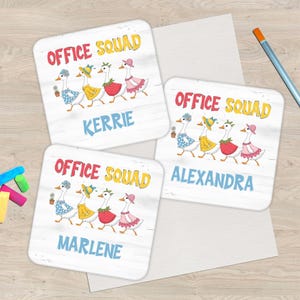 May include: Square coasters with a white wood grain background feature the text "OFFICE SQUAD" in yellow and red. Each coaster has a cartoon goose wearing a different outfit. Names "Kerrie", "Alexandra", and "Marlene" are printed on the coasters.