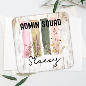 May include: A wooden sign with a whitewashed background and a rustic wood grain texture. The sign features a colorful design with vertical stripes of pink, gold, green, and pink. The stripes are decorated with watercolor-style flowers and leaves. The text "ADMIN SQUAD" is printed in black at the top of the sign, and the name "Stacey" is printed in black at the bottom of the sign.