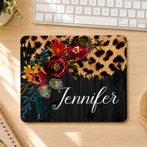 May include: A rectangular mouse pad featuring a split design with a leopard print pattern on the top half and a black wood grain texture on the bottom. A floral arrangement of red, orange, and green flowers sits on the left, with the name Jennifer.