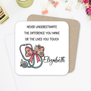May include: A white square coaster with rounded corners featuring the text "NEVER UNDERESTIMATE THE DIFFERENCE YOU MAKE OR THE LIVES YOU TOUCH." A stethoscope, floral bow, and the name "Elizabeth" are also on the coaster.