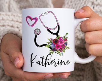 May include: White ceramic mug with a pink heart, a black stethoscope with a pink tube, a floral bouquet, and the name "Katherine" printed on the front.