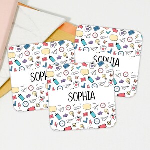 May include: Three white square coasters with a colorful doodle pattern of office supplies, including paper clips, light bulbs, envelopes, coffee cups, and airplanes. The name "Sophia" is printed on each coaster.