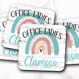 May include: Four square coasters with a white woodgrain background. Each coaster features a rainbow with a heart in the center and the text "Office Ladies" in black. The coasters are personalized with the name "Clarissa" in turquoise.