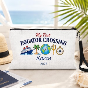 May include: A white zippered pouch with a black wrist strap featuring the text My First EQUATOR CROSSING, Karen, and 2027. The design includes a cruise ship, a palm tree, a globe marked 0 degrees, a golden trident, and a nautical compass.