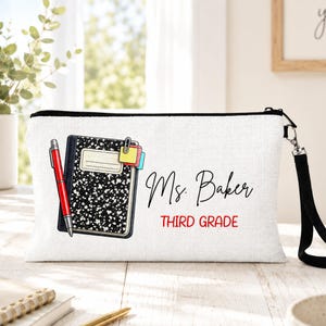 May include: A white rectangular zippered pouch featuring a black and white speckled composition notebook graphic, a red pen, and colorful sticky notes. The text Ms. Baker is printed in black script, with THIRD GRADE in red block letters below it.