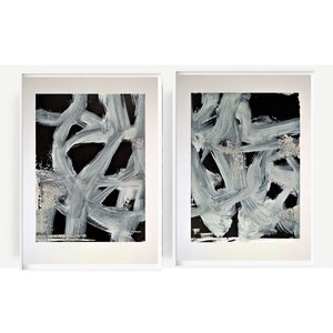 May include: Two framed abstract paintings with white brushstrokes on a black background.