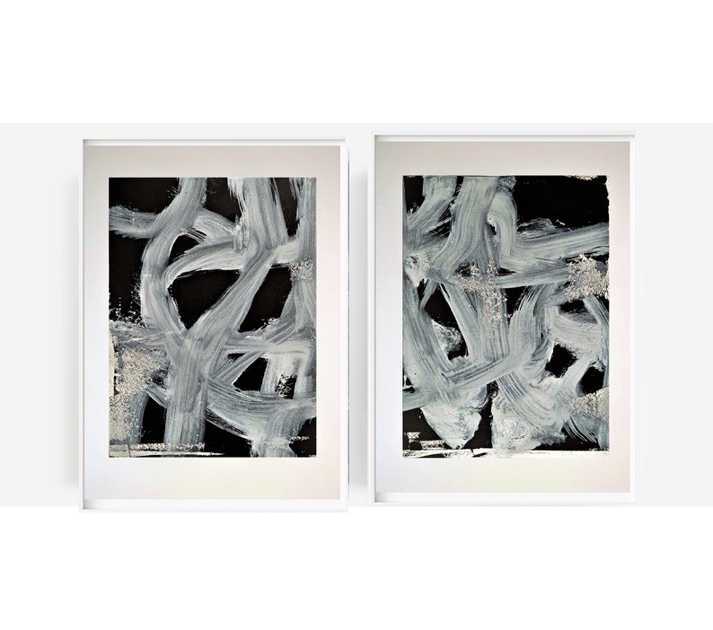 May include: Two framed abstract paintings with white brushstrokes on a black background.
