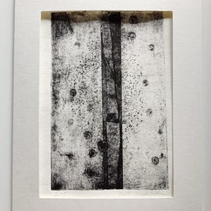 Könnte beinhalten: Schwarz-Weiß-Kunstdruck, gerahmt in einem weißen Passepartout. Das Kunstwerk zeigt einen zentralen vertikalen dunklen Streifen vor einem helleren Hintergrund mit kleinen dunklen Kreisen. Signiert und nummeriert.