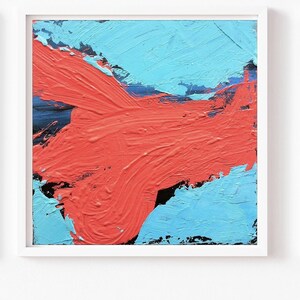 May include: Abstract art piece in a white frame. The artwork features bold brushstrokes of coral red over a light blue background. The painting has a textured appearance, with visible paint strokes.