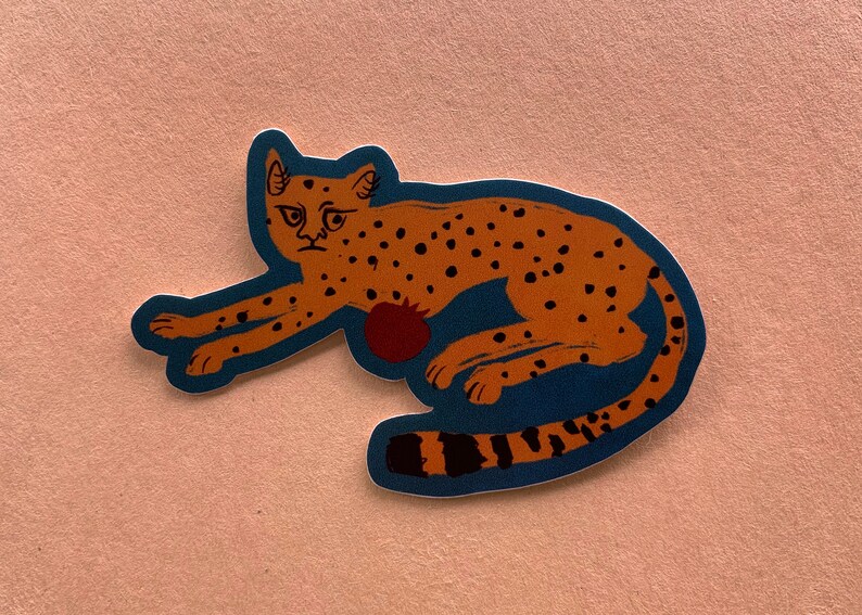 May include: A sticker of a brown and orange cheetah with black spots, lying down on a blue background. The cheetah has a red pomegranate on its side.