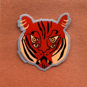 May include: A sticker featuring a cartoon tiger with multiple eyes, a red and orange color scheme, and the text "VIOLENT COSMOS" at the bottom.