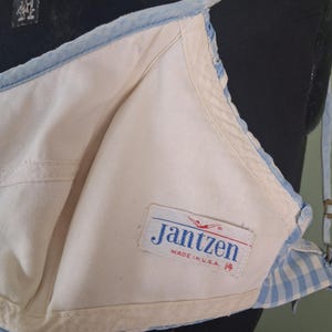 May include: Vintage Jantzen bra in cream and light blue. The bra features a classic design with a light blue trim and straps. The label reads "Jantzen MADE IN U.S.A. 14". The bra is displayed on a mannequin.