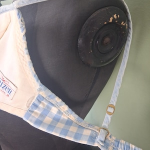 May include: A light blue and white gingham pattern top with adjustable straps. The top has a cream-colored interior and a label that reads "Katzen U.S.A.". The straps are a light blue color.