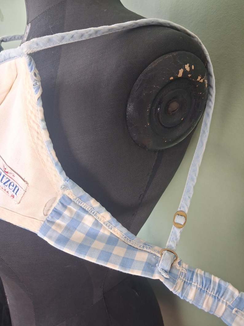 May include: A light blue and white gingham pattern top with adjustable straps. The top has a cream-colored interior and a label that reads "Katzen U.S.A.". The straps are a light blue color.
