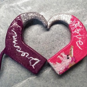 Pode incluir: Duas capas para aparelho auditivo em forma de metades de coração, uma roxa com a palavra dream e uma rosa com um gráfico de unicórnio e a palavra love. Cada peça possui um fecho magnético circular ligado por um fio fino à caixa em coração.