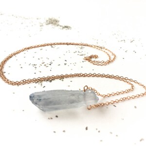 Puede incluir: Un delicado collar de cadena de oro rosa con un colgante de cristal de cuarzo transparente. El cristal es una punta natural, en bruto y sin pulir.