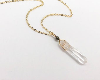 May include: A gold chain necklace with a clear quartz crystal pendant and a small black bead.