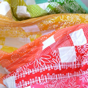May include: A colorful patchwork quilt with a variety of floral and geometric patterns. The quilt features shades of red, orange, yellow, green, and blue, with white accents. The quilt is made of soft fabric and has a quilted design.