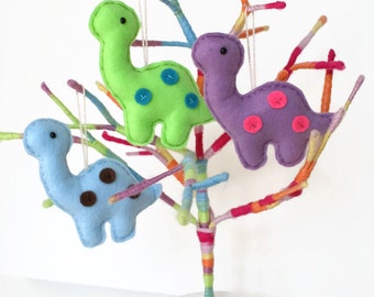 May include: Three felt dinosaur ornaments hanging from a colorful yarn tree. The dinosaurs are green, purple, and blue with button eyes and spots.