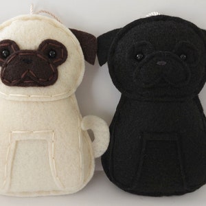 May include: Two felt pug dog ornaments, one is black and one is cream colored.
