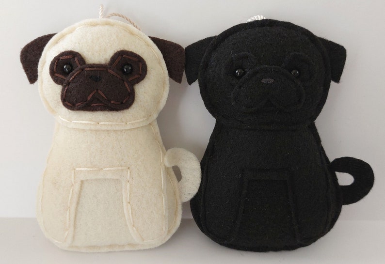 May include: Two felt pug dog ornaments, one is black and one is cream colored.