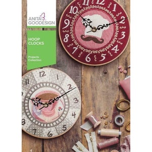 May include: Two embroidery hoop clocks, one with a red background and a chef's hat design, the other with a gray background and a coffee cup design. The clocks are on a wooden surface with sewing supplies.