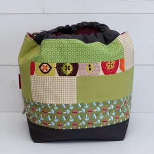 Könnte beinhalten: Eine grüne, braune und weiße Patchwork-Kordeltasche mit einem Pilzdruck auf dem Boden. Die Tasche ist aus Stoff und hat einen Kordelverschluss.