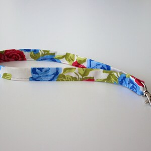 Könnte beinhalten: Ein weißes Stoffband mit einem Blumenmuster aus roten, blauen und grünen Rosen. Das Band hat einen silbernen Metallclip.