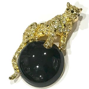 May include: A gold-tone brooch featuring a jeweled leopard perched atop a black cabochon.