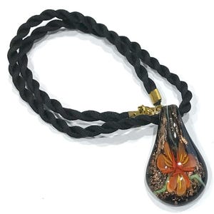 May include: A black rope necklace with a teardrop-shaped pendant. The pendant is dark with an orange flower design and gold accents. The necklace has a gold clasp.
