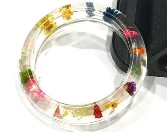 May include: A clear resin bangle bracelet with embedded pressed flowers in shades of pink, yellow, orange, blue, and green.