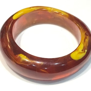 Pode incluir: Um bracelete rígido vermelho e amarelo com veios. O bracelete é feito de um material liso e brilhante.