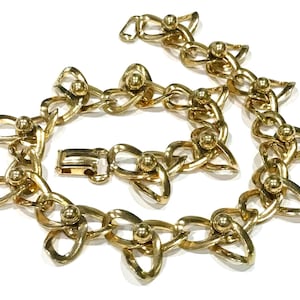 May include: A gold-toned necklace with a unique design. The necklace features interlocking links with a knot-like shape, each adorned with a small, round bead. A secure clasp is visible. The jewelry is displayed against a white background.