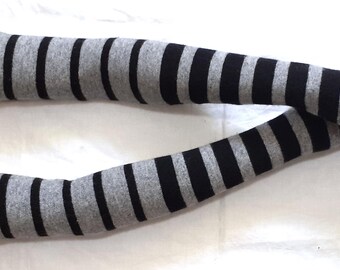 May include: A pair of gray and black striped arm warmers. The arm warmers are made of a soft material and have a fingerless design. The stripes are evenly spaced and run horizontally along the length of the arm warmers.