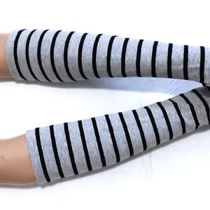 May include: Gray and black striped arm warmers. These fingerless gloves are gray with evenly spaced black stripes. The arm warmers are displayed on a mannequin arm against a white background.